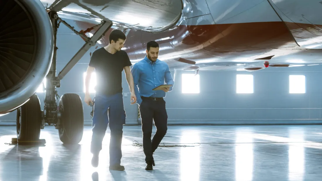 Aircraft maintenance engineer showing technical data on a tablet to a technician beside an airliner in a hangar