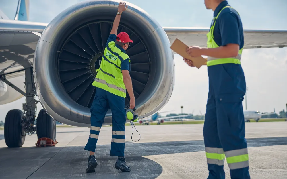 Two aircraft maintenance engineers examining a jet engine on the apron, one holding a clipboard