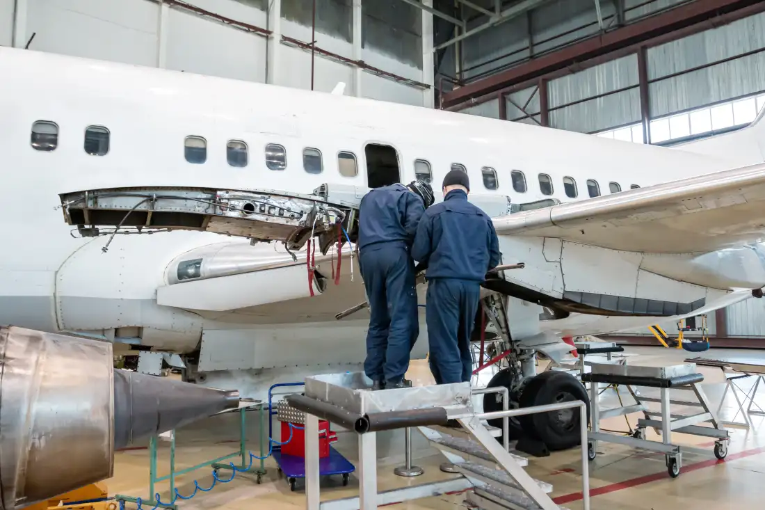 Passenger aircraft inside a maintenance hangar with engineers working beside the engine