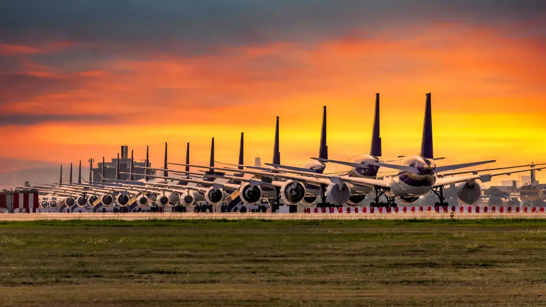 Row of commercial airliners parked in a line at an airport at sunset