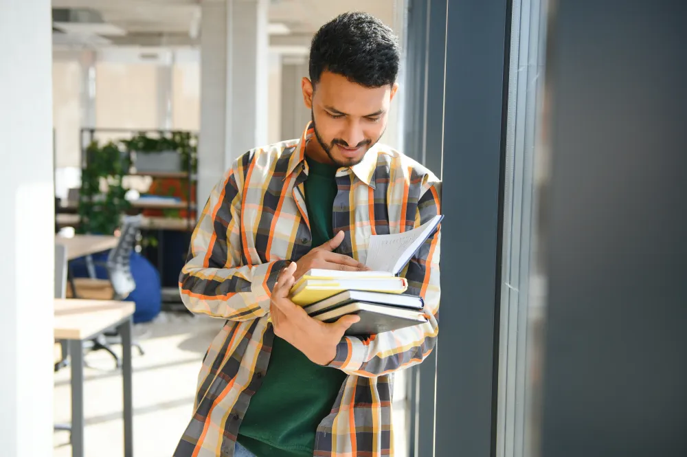 Young man studying from a textbook in a college library, preparing for an EASA Part-66 module exam