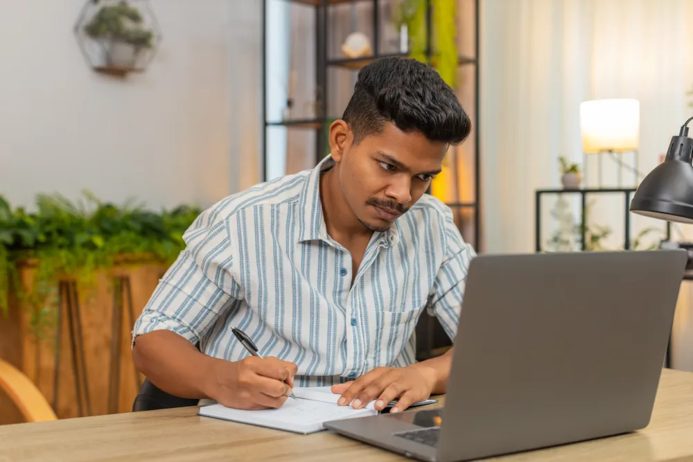 Man taking notes at a laptop while completing an online test, similar to sitting a Part-66 module exam
