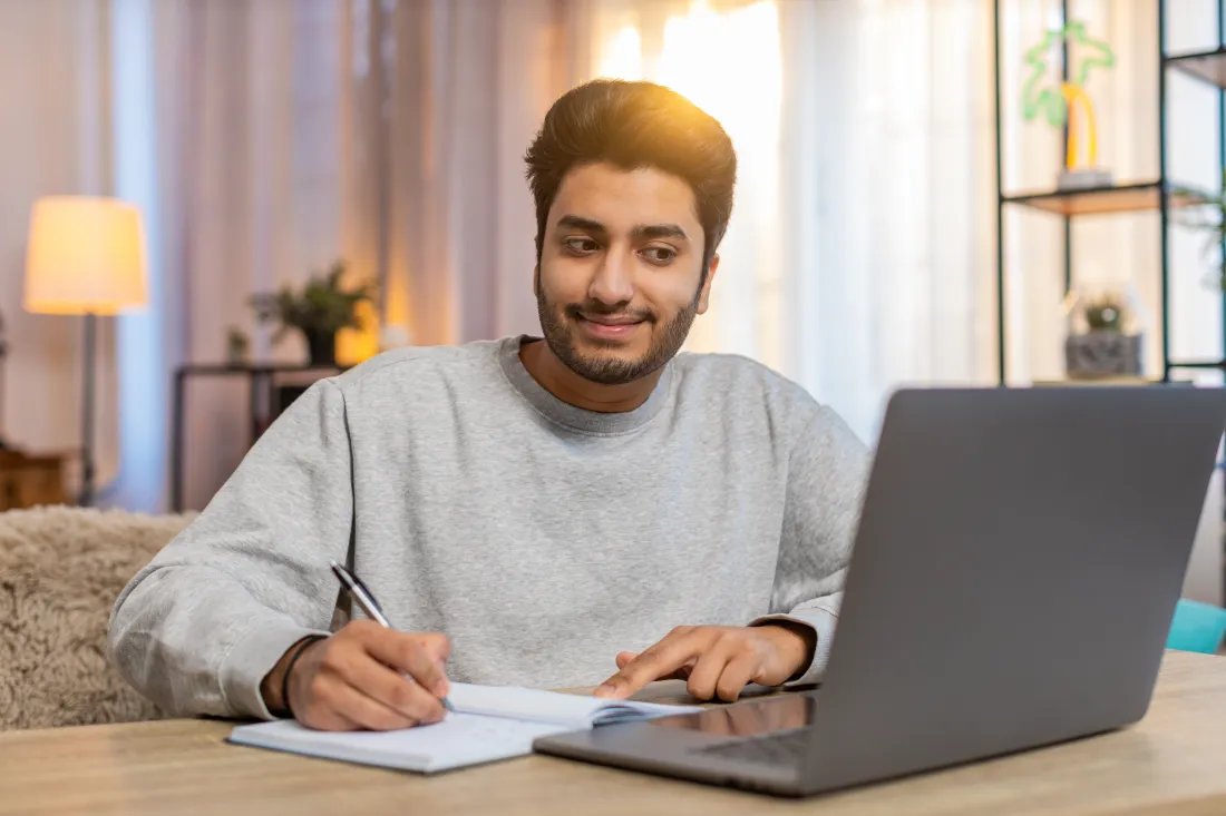 Student taking notes beside a laptop while studying for module exams