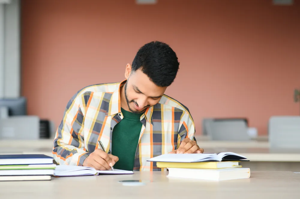 South Asian trainee writing notes at a study desk while preparing for a module exam