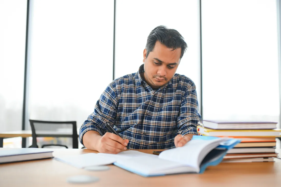 South Asian student studying at a desk with open books