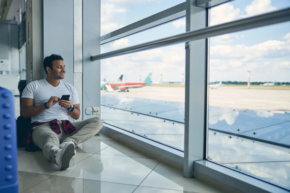Young man watching airplanes through an airport terminal window while choosing a career route